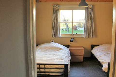 Chambre avec deux lits simples, table de nuit, lampe et fenêtre au Holiday Home 3 Aarde Green Camping Lage Zwaluwe, Pays-Bas.