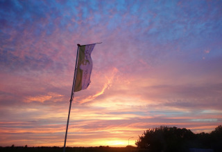 Cielo al atardecer con nubes de colores y bandera en Holiday Home 3 Aarde Green Camping Lage Zwaluwe, Países Bajos.