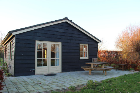 Zwarte houten lodge met beige deur en raam, terras met picknickbank bij Holiday Home 3 Aarde Green Camping Lage Zwaluwe, Nederland.