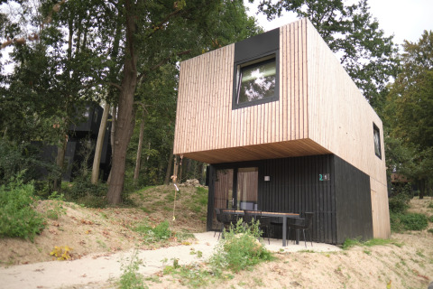 Moderne houten lodge bij Resort Gulpen 7, omgeven door bomen, met zithoek voor de ingang.