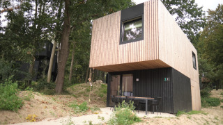 Lodge moderne en bois au Resort Gulpen 7, entouré d’arbres, avec terrasse et sièges devant l’entrée.
