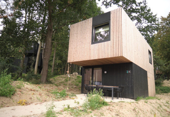 Moderne houten lodge bij Resort Gulpen 7, omgeven door bomen, met zithoek voor de ingang.