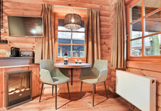 Cozy corner in wooden chalet Park Duc de Brabant 3 in the Netherlands with dining table, fireplace, windows.