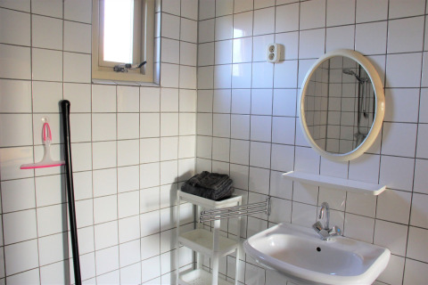 Helles Badezimmer mit weißen Fliesen, Spiegel, Waschbecken und Regal im Holiday Home in den Niederlanden.