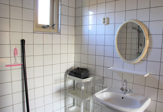 Helles Badezimmer mit weißen Fliesen, Spiegel, Waschbecken und Regal im Holiday Home in den Niederlanden.
