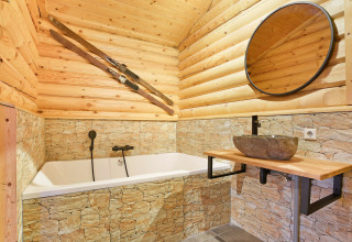 Rustikt badeværelse i træ og sten på Park Duc de Brabant 3 chalet i Holland, set med badekar og ski.