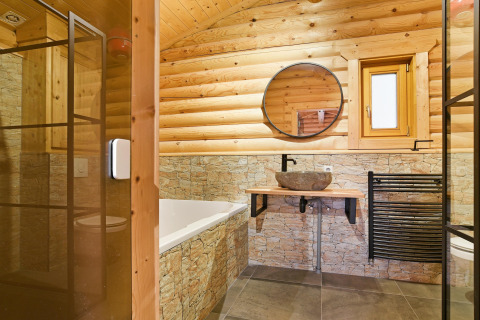 Baño de chalet moderno con paredes de madera y piedra, espejo redondo y lavabo de piedra en Países Bajos.