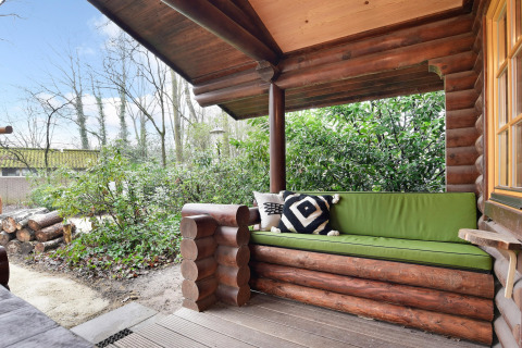 Udendørs veranda med træbænk og grøn hynde i chalet Park Duc de Brabant 3, Holland, omgivet af natur.