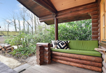 Veranda coperta con panca di legno e cuscino verde nello chalet Park Duc de Brabant 3, Paesi Bassi, immerso nella natura.