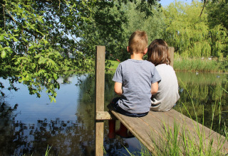 Due bambini seduti su un molo di legno presso un lago a Holiday Home 3 Aarde Green Camping Lage Zwaluwe, Paesi Bassi.
