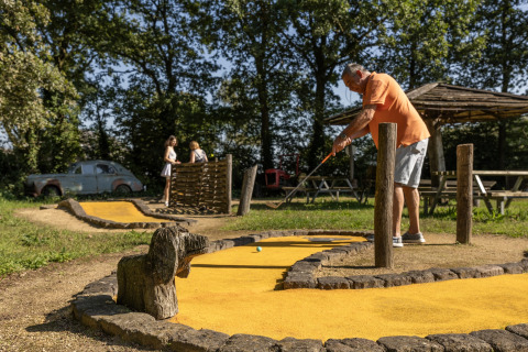 En mand spiller minigolf i det fri ved Park Duc de Brabant 3, Holland, med to kvinder i baggrunden.