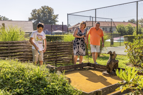Familie spiller minigolf udendørs i solen ved Park «Duc de Brabant 3» i Holland, tæt ved tennisbaner.