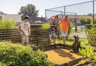 Family playing outdoor mini golf in the sunshine at Park «Duc de Brabant 3» in the Netherlands, near tennis courts.