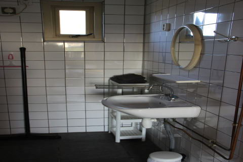 Modern bathroom with white tiled walls, a sink, round mirror, towel rack, and a small upper window.