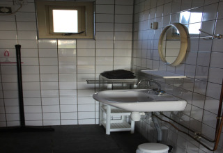 Moderne badkamer met witte tegels, wastafel, ronde spiegel, handdoekrek en klein bovenraam.