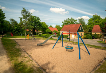 Legeplads med sand, gynger og rutsjebane foran charmerende chaletter i Park Duc de Brabant, Holland.