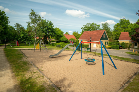 Playground with sand, a swing, and slide in front of cozy chalets at Park Duc de Brabant, Netherlands.