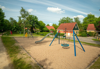 Parco giochi con sabbia, altalena e scivolo davanti a chalet nel Park Duc de Brabant, Paesi Bassi.