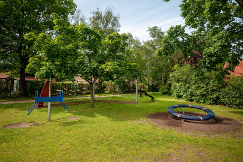 Children’s playground in lush park at Park «Duc de Brabant 3» chalet in the Netherlands, with slide and roundabout.