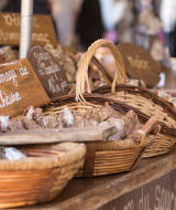 Puesto de mercado con cestas de embutidos y carteles escritos a mano en un mercado francés.