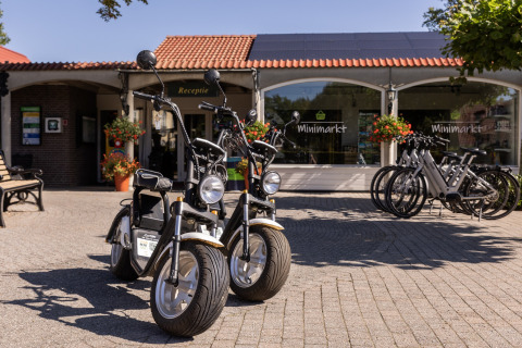 Two electric scooters and several bikes parked outside the minimarket at Park Duc de Brabant 3, Netherlands.