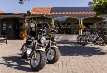 Due scooter elettrici e diverse biciclette davanti al minimarket di Park Duc de Brabant 3, Paesi Bassi.