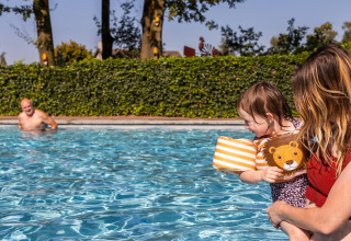 Toddler with floaties and adult in swimming pool, man in background, Park Duc de Brabant 3, Netherlands.