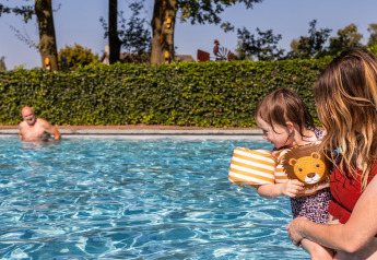 Bimbo con braccioli e adulto in piscina, uomo sullo sfondo, Park Duc de Brabant 3, Paesi Bassi.