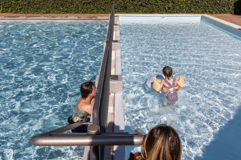 To voksne og et barn leger i delt swimmingpool i Park Duc de Brabant 3, Holland, på en solskinsdag.