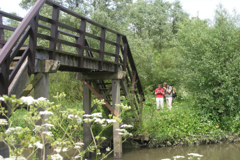 Zwei Personen stehen unter einer Holzbrücke auf einem grünen Campingplatz in Lage Zwaluwe, Niederlande.