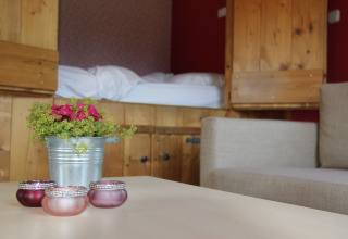 Camera accogliente con armadi in legno, letto, divano beige, vaso di fiori e portacandele.