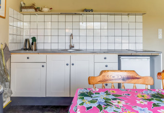 Coin cuisine du Holiday Home 3 Aarde Green Camping Lage Zwaluwe avec carrelage blanc et chaises en bois.