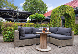 Udendørs loungeområde ved Park Duc de Brabant 3 i Holland med sofaer, bord, vin og grønne hække.