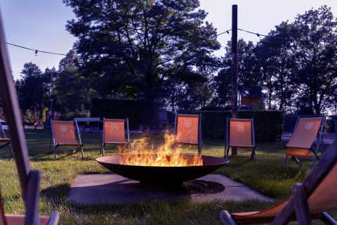Outdoor fire pit surrounded by orange chairs in a green park at Park «Duc de Brabant 3» in the Netherlands.