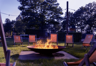 Outdoor fire pit surrounded by orange chairs in a green park at Park «Duc de Brabant 3» in the Netherlands.