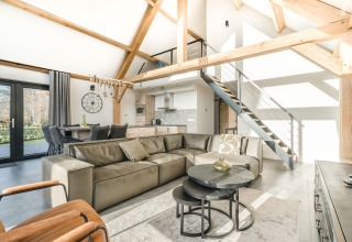 Lyst og moderne opholdsstue i en lodge med synlige bjælker, lædersofa og åben hems i Park de Kievit 22.