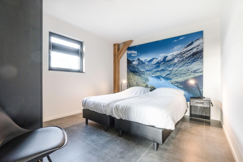 Soveværelse på Park de Kievit 22-lodge i Belgien med to senge og bjerglandskab på væggen.