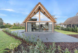 Moderne lodge med stort glasparti og stråtækt tag i Park de Kievit 22, smukke omgivelser i Belgien.