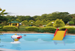 Piscina infantil al aire libre con tobogán amarillo y figura de payaso en alojamiento glamping rodeado de verde.