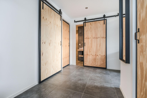 Moderne gang i Park «de Kievit 22» lodge i Belgien med skydedøre af lyst træ og grå flisegulve.