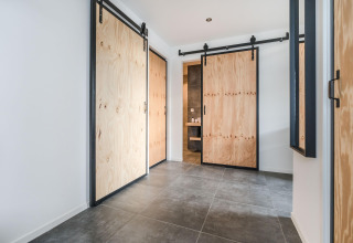 Moderne gang i Park «de Kievit 22» lodge i Belgien med skydedøre af lyst træ og grå flisegulve.