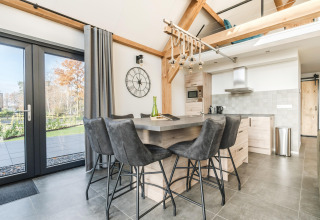 Moderne køkken og spiseområde i Park de Kievit 22-lodgen i Belgien med store vinduer og grå stole.