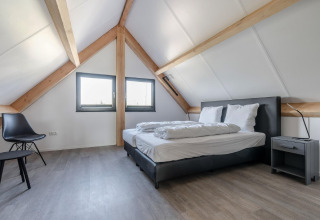 Dormitorio moderno en el ático del chalet Park de Kievit 19 en Bélgica, con vigas vistas y cama doble.