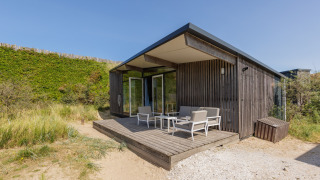Sea Lodges Bloemendaal 5, modern houten lodge met terras en stoelen, te midden van zandduinen en natuur.
