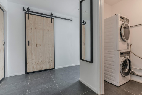 Lavandería en el chalet Park de Kievit 19 en Bélgica con puerta corrediza, espejo y lavadoras apiladas.