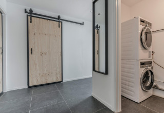 Lavandería en el chalet Park de Kievit 19 en Bélgica con puerta corrediza, espejo y lavadoras apiladas.