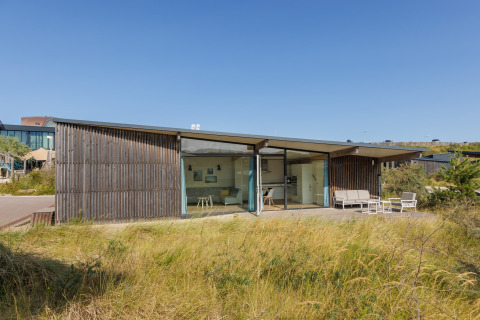 Modern strandhuis Sea Lodges Bloemendaal 4 met glazen gevel en terras, omgeven door zon en duingras.
