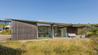 Modern strandhuis Sea Lodges Bloemendaal 4 met glazen gevel en terras, omgeven door zon en duingras.