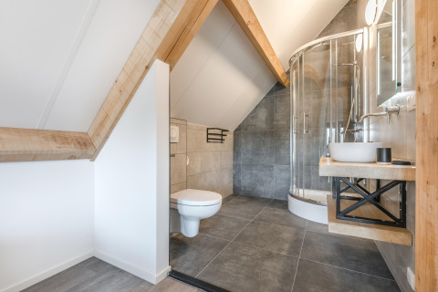 Moderne badeværelse med skrå lofter, trægulve, hjørnebruser og væghængt toilet på Park de Kievit 22.