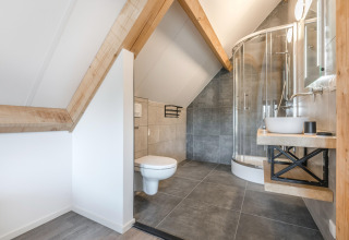 Moderne badeværelse med skrå lofter, trægulve, hjørnebruser og væghængt toilet på Park de Kievit 22.